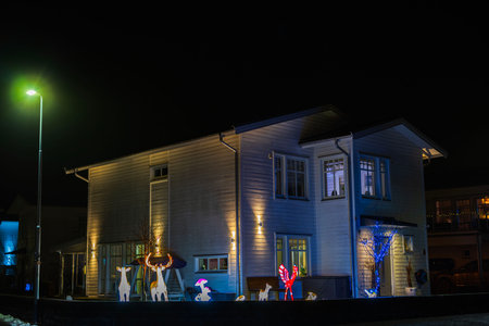 Modern wooden villa illuminated at night with festive outdoor Christmas decorations, including glowing reindeer, mushrooms and colorful lights.のeditorial素材