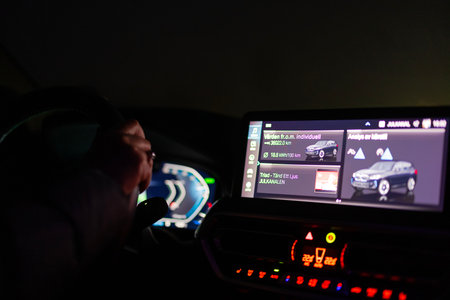 Driver operating BMW iX3 electric car at night, focusing on illuminated infotainment display and digital dashboard showing energy consumption details.のeditorial素材