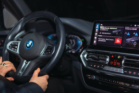 Interior of BMW iX3 electric car showing illuminated steering wheel controls, digital dashboard and advanced infotainment system display at night.のeditorial素材