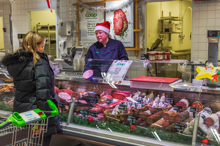 Butcher in Santa hat serving customer at festive deli counter with assorted meats and holiday decorations.のeditorial素材
