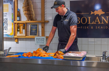Seafood chef slicing fresh salmon fillets at fish counter in store with wooden decor and allergy information sign.のeditorial素材