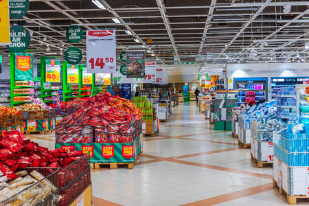 Supermarket aisle with stacked products, promotional signs, colorful displays, and organized shelves under bright lighting.のeditorial素材