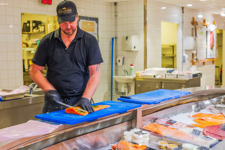 Fishmonger slicing fresh salmon fillet on blue cutting board at seafood counter in grocery store.のeditorial素材