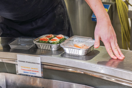 Seafood counter with prepared shrimp dishes in aluminum trays on stainless steel surface at grocery store.のeditorial素材