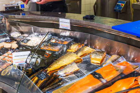 Variety of smoked and fresh fish displayed at seafood counter in grocery store with price tags and labels. Sweden.のeditorial素材