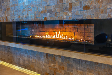 Modern linear gas fireplace with vibrant flames set against textured stone wall in cozy interior space.の写真素材