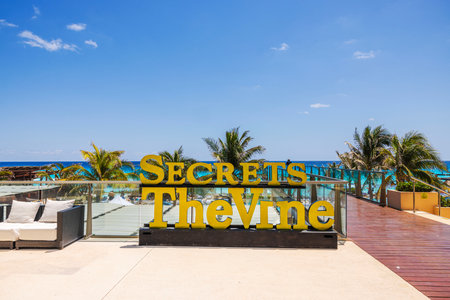 Scenic view from Secrets The Vine resort with bright yellow sign, palm trees, turquoise Caribbean sea and clear blue sky. Mexico. Cancun.のeditorial素材