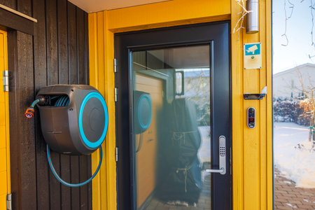 Close-up view of modern house entrance with yellow facade, glass door, smart lock, garden hose reel and security camera.の写真素材