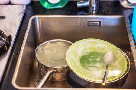 Dirty dishes in stainless steel kitchen sink with leftover food and soapy water, showing everyday home cleaning routine.の写真素材
