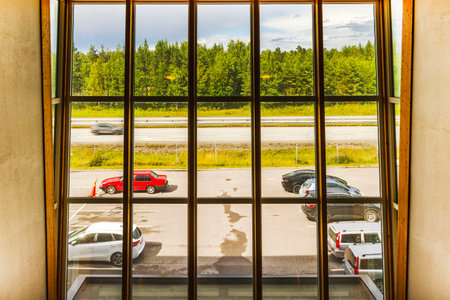 Large panoramic window view showing highway with cars, parking lot and green forest under cloudy sky.のeditorial素材