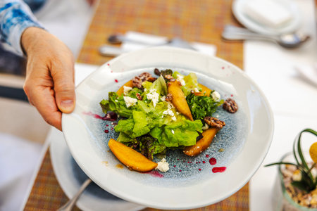 Close-up view of fresh salad with green lettuce, peach slices, nuts and cheese served on white plate with sauce drizzle.の写真素材