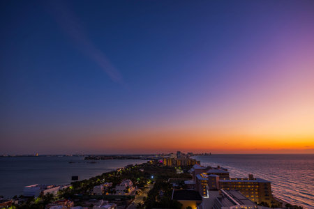 Scenic view of the Caribbean Sea coastline at sunset with vibrant orange and purple sky over illuminated hotels and calm water. Mexico. Cancun.の写真素材