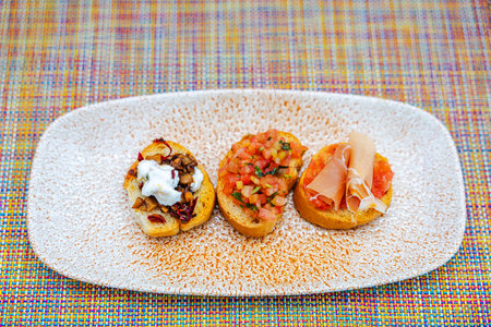 Close-up view of three bruschetta appetizers on textured plate with colorful woven tablecloth background.の写真素材