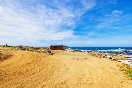 Coastal desert landscape with rustic wooden shelter overlooking Caribbean Sea under bright blue sky. Aruba.の写真素材