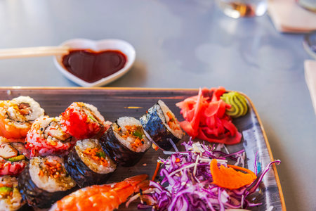 Assorted sushi rolls with pickled ginger, wasabi and soy sauce served on wooden platter in vibrant presentation.の写真素材