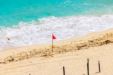 Red flag on sandy beach with turquoise waves indicating caution for swimmingの写真素材