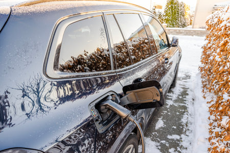 Electric vehicle charging outdoors during snowy winter day near hedge in residential driveway.の写真素材