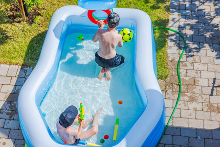 Children playing in an inflatable pool with toys on sunny summer day in backyard. の写真素材