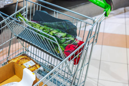 Shopping cart with fresh red roses and various packaged groceries placed on tiled floor in supermarket. Sweden.の写真素材