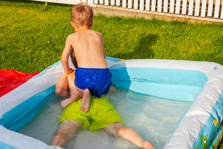 Children enjoying an inflatable pool on sunny day in grassy backyard near white picket fence. Sweden.の写真素材