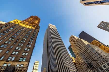 Towering skyscrapers in Midtown Manhattan reflecting golden sunlight against clear blue sky on bright spring afternoon.の写真素材