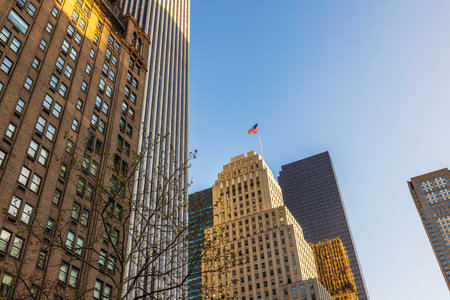 Illuminated skyscrapers of Manhattan with American flag waving on top against clear blue sky on spring evening. New York. USA.の写真素材