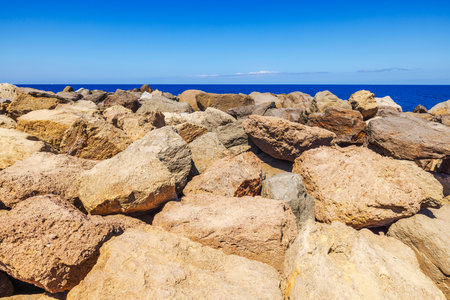 Large rugged coastal rocks against deep blue ocean horizon under clear sunny sky. Gran Canaria, Las Palmas, Spain.の写真素材