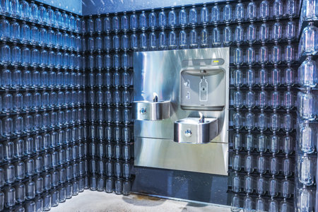 Modern stainless steel drinking fountains with refill station against wall of empty glass bottles. New York. USA.の写真素材