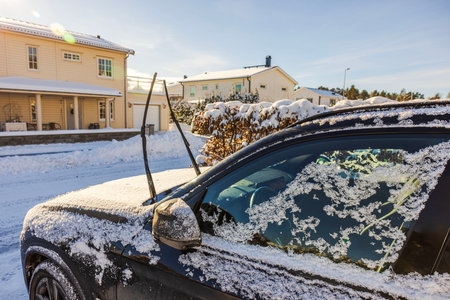 Frozen black car with raised windshield wipers covered in snow near residential house on cold winter day. Sweden.の写真素材