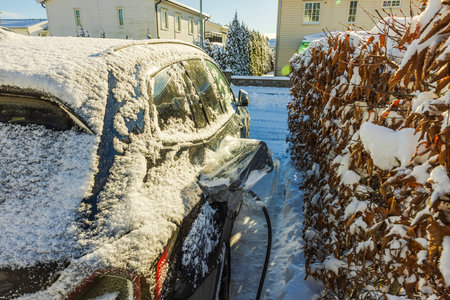 Electric car covered in snow charging at charging station with plastic cover protecting charging port. Sweden.の写真素材