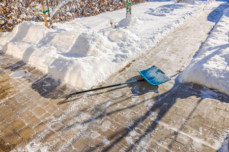 Snow shovel lying on cleared brick pathway in winter garden near villa entrance. Sweden.の写真素材