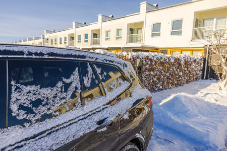 Frozen electric car parked near modern townhouse covered in snow on bright winter day. Sweden.の写真素材