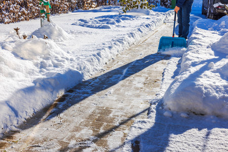 Man clearing snow from brick pathway in winter garden near villa entrance. Sweden.の写真素材