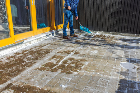 Person clearing snow from brick patio with blue plastic shovel during sunny winter afternoon. Sweden.の写真素材