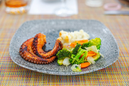 Grilled octopus served with steamed vegetables and mashed potatoes on textured plate at restaurant table. Mexico.の写真素材