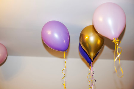 Close-up view of colorful helium balloons floating near ceiling indoors.の写真素材