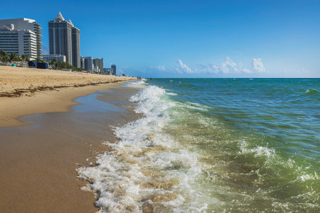 Emerald green waves of Atlantic Ocean rolling onto sandy shore in Miami Beach with high-rise hotels in background. Miami Beach. USA.の写真素材