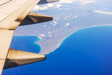 Aerial view of airplane wing over Caribbean Sea coastline with blue water and clouds.の写真素材