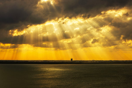 Dramatic golden sunlight breaking through heavy clouds over calm Caribbean sea, casting glowing rays on water and distant horizon. Mexico. Cancun.の写真素材