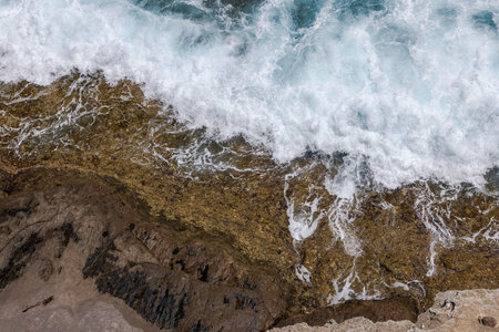 Waves crashing against rocky shoreline of Atlantic Ocean on Gran Canaria, foamy water swirling over textured rocks.の写真素材