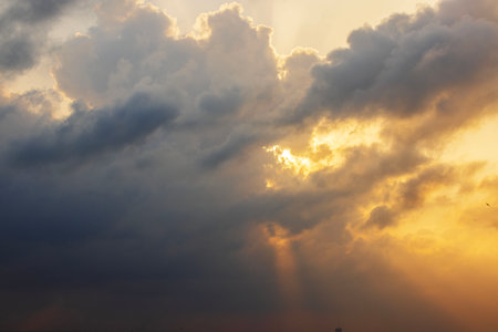 Dramatic sunset sky with dark storm clouds and golden sun rays breaking through.の写真素材