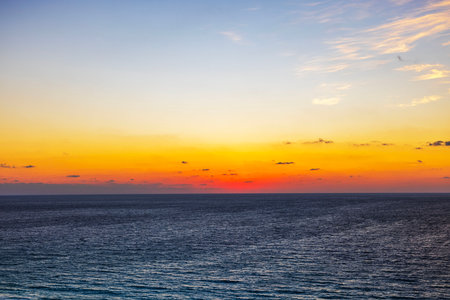Golden sunrise over calm Caribbean Sea with vibrant orange and blue gradient sky and scattered clouds. Mexico.の写真素材