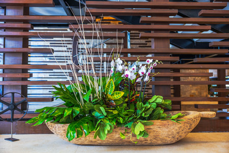 Close up view of tropical floral arrangement with orchids and green leaves in rustic wooden bowl indoors. Mexico.の写真素材