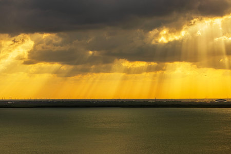 Golden sun rays breaking through dramatic storm clouds over calm sea at sunset.の写真素材
