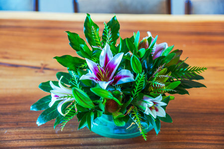 Close up view of bouquet with blooming lilies and fresh green leaves in glass bowl on wooden table. Mexico.の写真素材