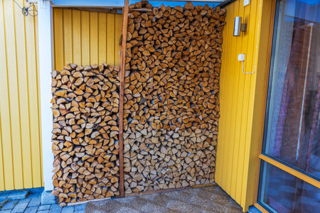 Firewood stacked against yellow wooden wall near panoramic glass window of villa for winter heating. Sweden.の写真素材