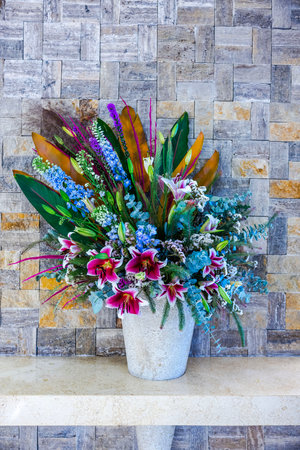 Bright flower bouquet in stone vase against decorative brick wall with mixed colorful flowers.の写真素材