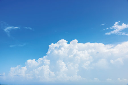 White cumulus clouds rising above horizon against clear blue sky on hot summer day.の写真素材