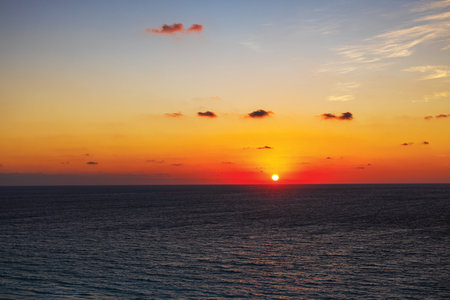 Orange sunset over calm sea with clouds glowing in the sky on peaceful evening.の写真素材
