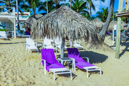 Two white loungers with purple towels under straw umbrella on clean sand near Atlantic Ocean. Dominican Republic. Punta Cana.の写真素材